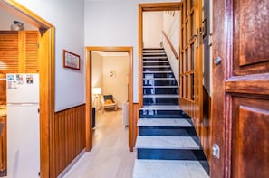 A hallway with a wooden door, a refrigerator with magnets, a chair, and a staircase with a wooden railing.