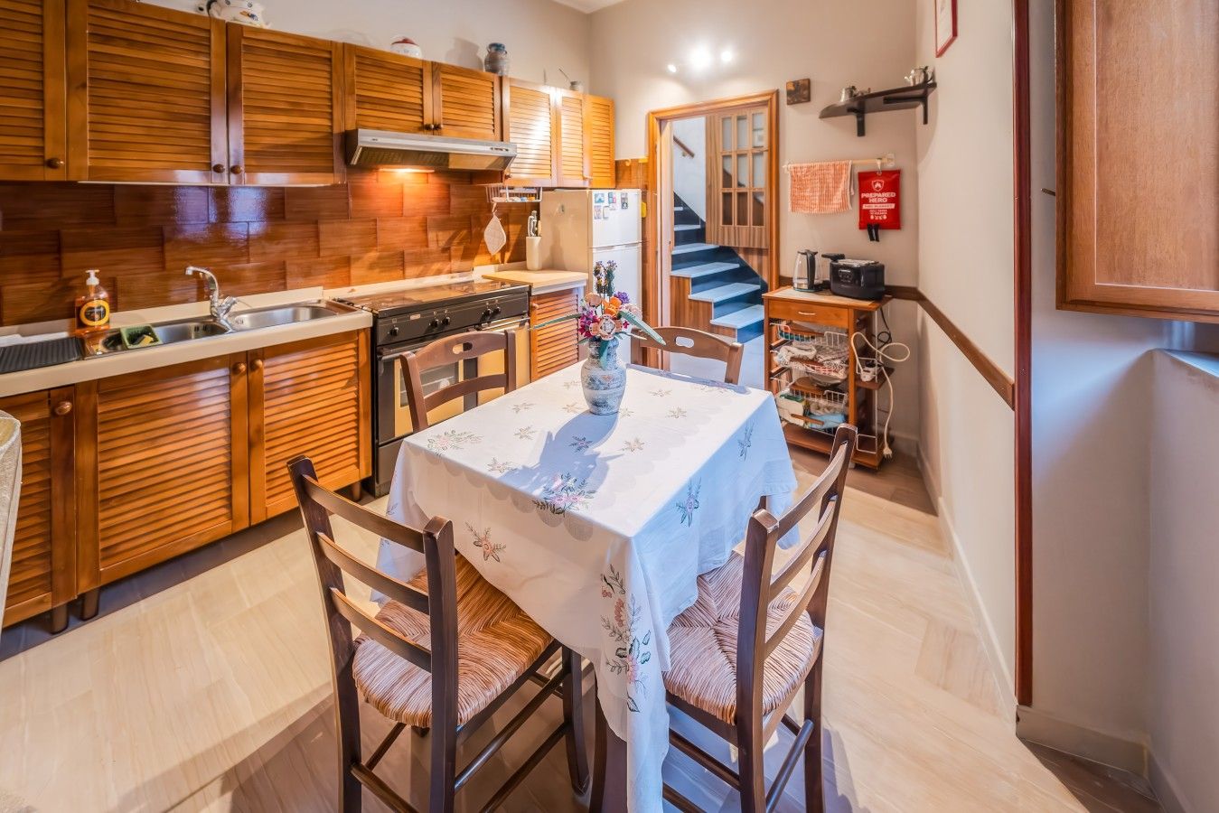 Une cuisine avec des meubles en bois, une table à manger avec des chaises et un escalier menant à un autre niveau.