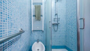 Une salle de bain avec un lavabo blanc, une serviette suspendue à un porte-serviettes et un espace douche.
