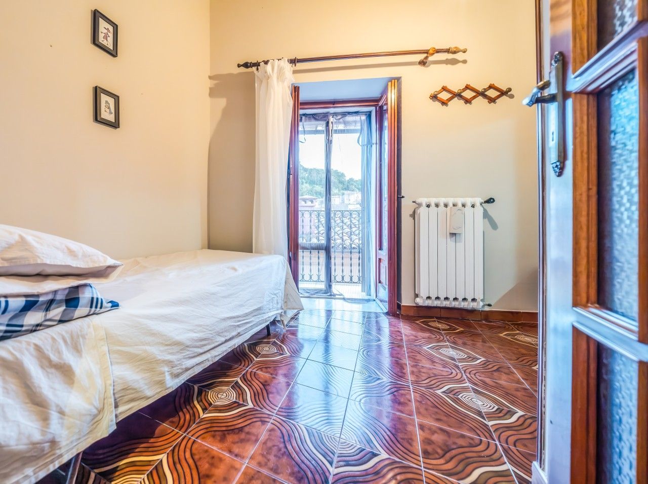 Une pièce avec un lit, un radiateur et une vue sur l’extérieur, visible à travers une porte.