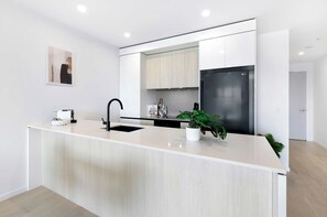 A modern kitchen with a central island, a built-in sink, and a stainless steel refrigerator. - Ocean View 2BR, Steps to Beach | Pool, Gym Parking (Broadbeach)