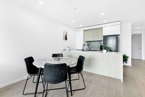 A modern kitchen with a marble island, black chairs, and a white dining table. - Ocean View 2BR, Steps to Beach | Pool, Gym Parking (Broadbeach)