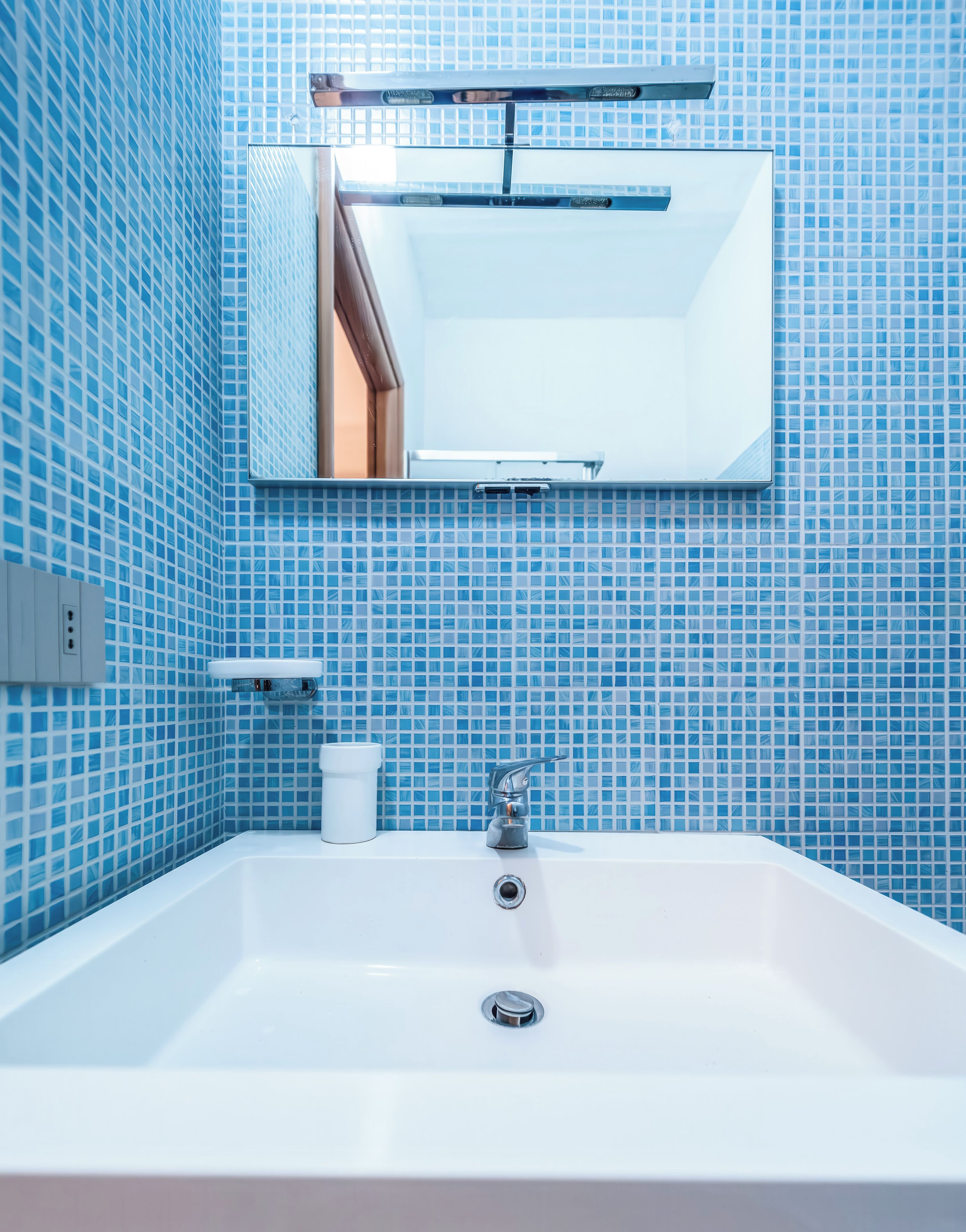 Ein Badezimmer mit Waschbecken, Spiegel und blauen Fliesenwänden.