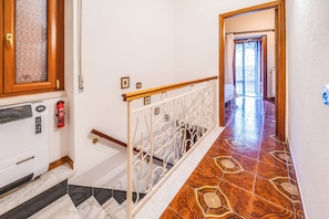 A hallway with a wooden door, a fire extinguisher, a radiator, and a patterned floor. - Casa Bisaccese (Bisaccia)