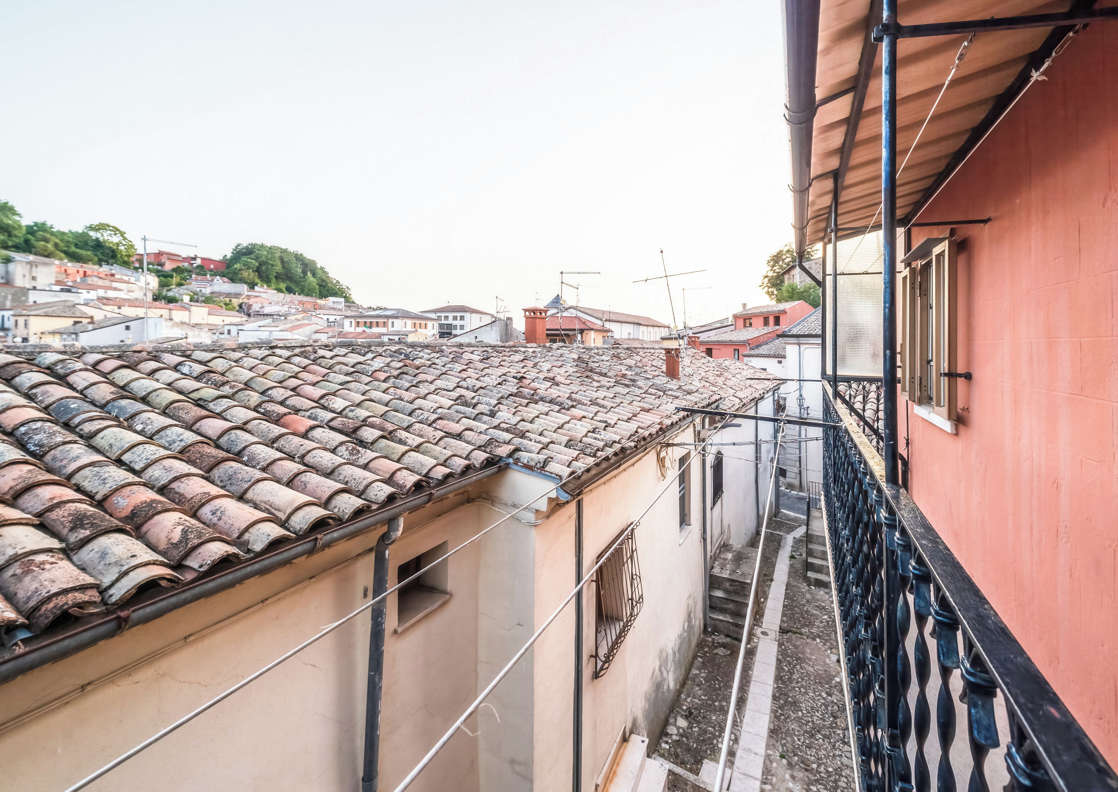 A narrow alleyway with a tiled roof, a red building on the right, and a view of other buildings in the distance.