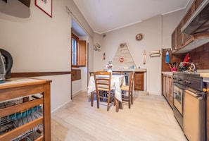A kitchen with wooden cabinets, a stove, and a dining area with chairs and a table. - Casa Bisaccese (Bisaccia)