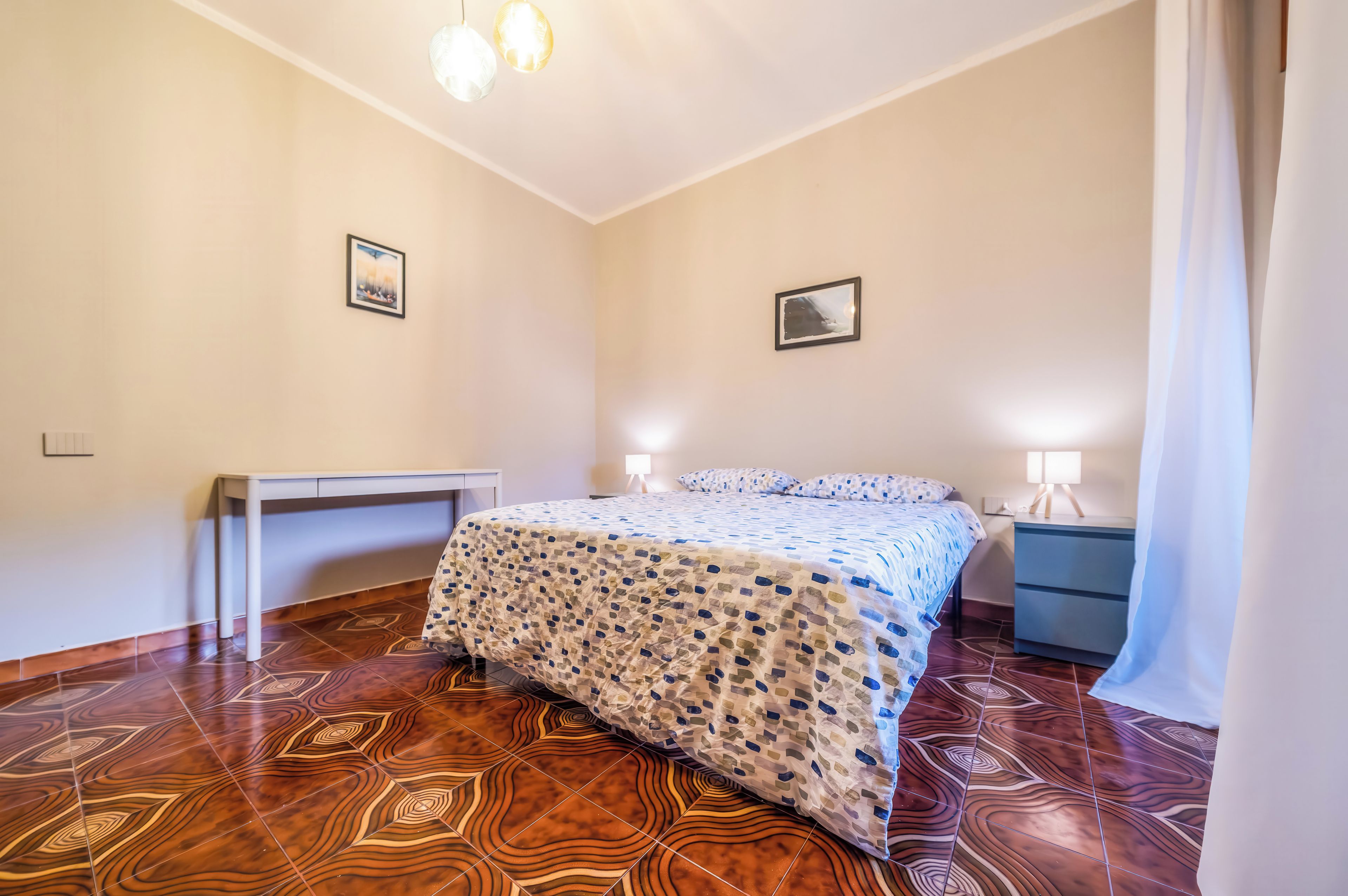 Een slaapkamer met een bed, nachtkastjes, een bureau en vloerbekleding met een patroon.