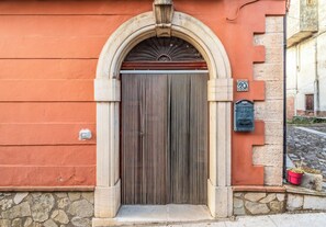 A building with a stone facade, a wooden door with vertical slats, and a small mailbox on the right. - Casa Bisaccese (Bisaccia)