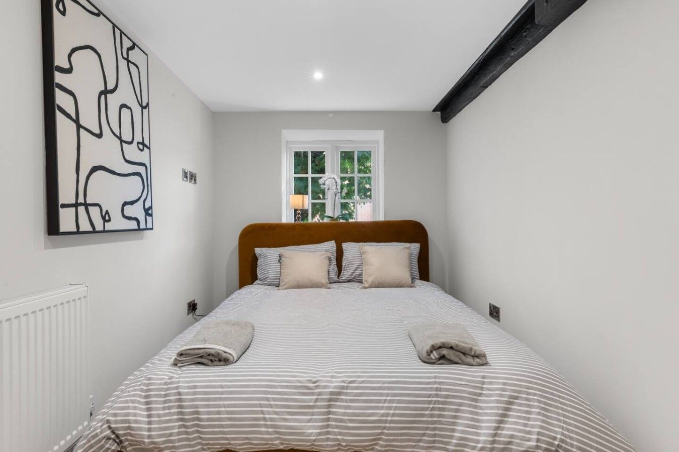 A bedroom with a bed, a window, a radiator, and a wall art piece.