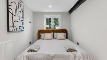 A bedroom with a bed, a window, a radiator, and a wall art piece.