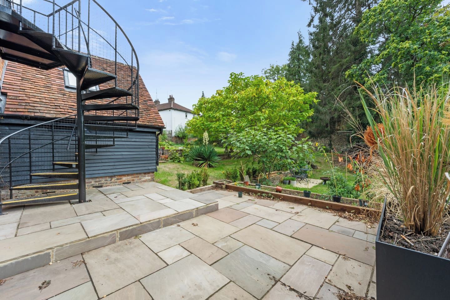 A residential backyard with a spiral staircase, a garden with various plants, and a brick wall.