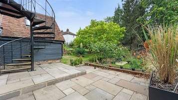 A residential backyard with a spiral staircase, a garden with various plants, and a brick wall.