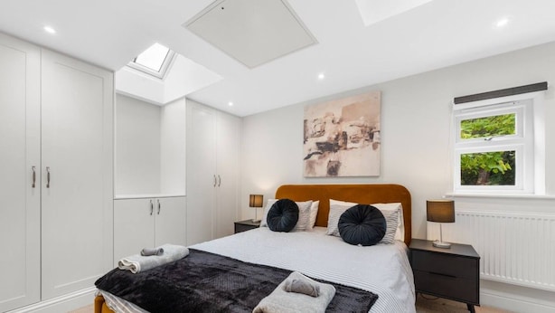 A bedroom with a bed, bedside tables, a window with a view, and a skylight. - Modern & Historic Mill Flat With Garden View (Surrey)