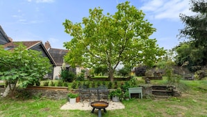A garden with a tree, a table, and chairs. There is a stone wall and a building in the background. - Modern & Historic Mill Flat With Garden View (Surrey)
