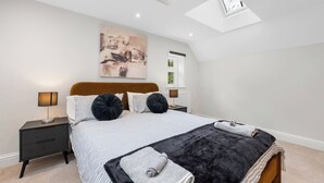 A bedroom with a bed, bedside tables, a skylight, and a painting on the wall. - Modern & Historic Mill Flat With Garden View (Surrey)