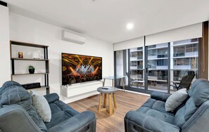 Ein modernes Wohnzimmer mit großem Flachbildfernseher, einer Couch, einem Couchtisch und einem Bücherregal.