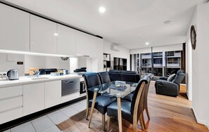 Une cuisine moderne avec un coin repas, comprenant une table en verre et des chaises en cuir noir.