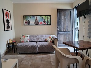 Una sala de estar con un sofá, una mesa de comedor, un televisor y una puerta.