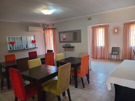 Un comedor con una mesa y sillas, un televisor montado en la pared y una ventana con cortinas.