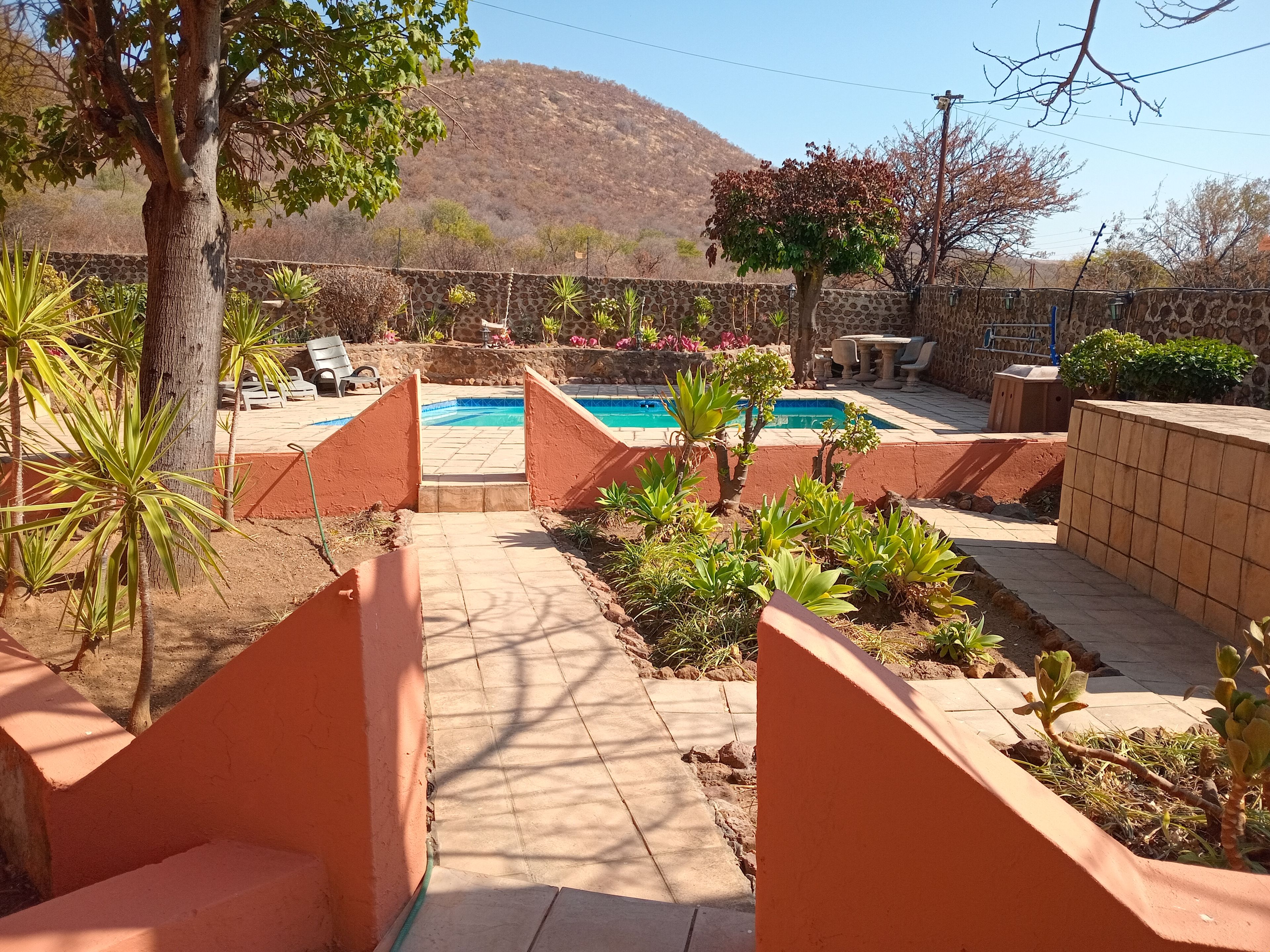 A pool area with a stone wall, plants, and a view of a hill.