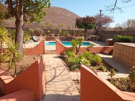 A pool area with a stone wall, plants, and a view of a hill.