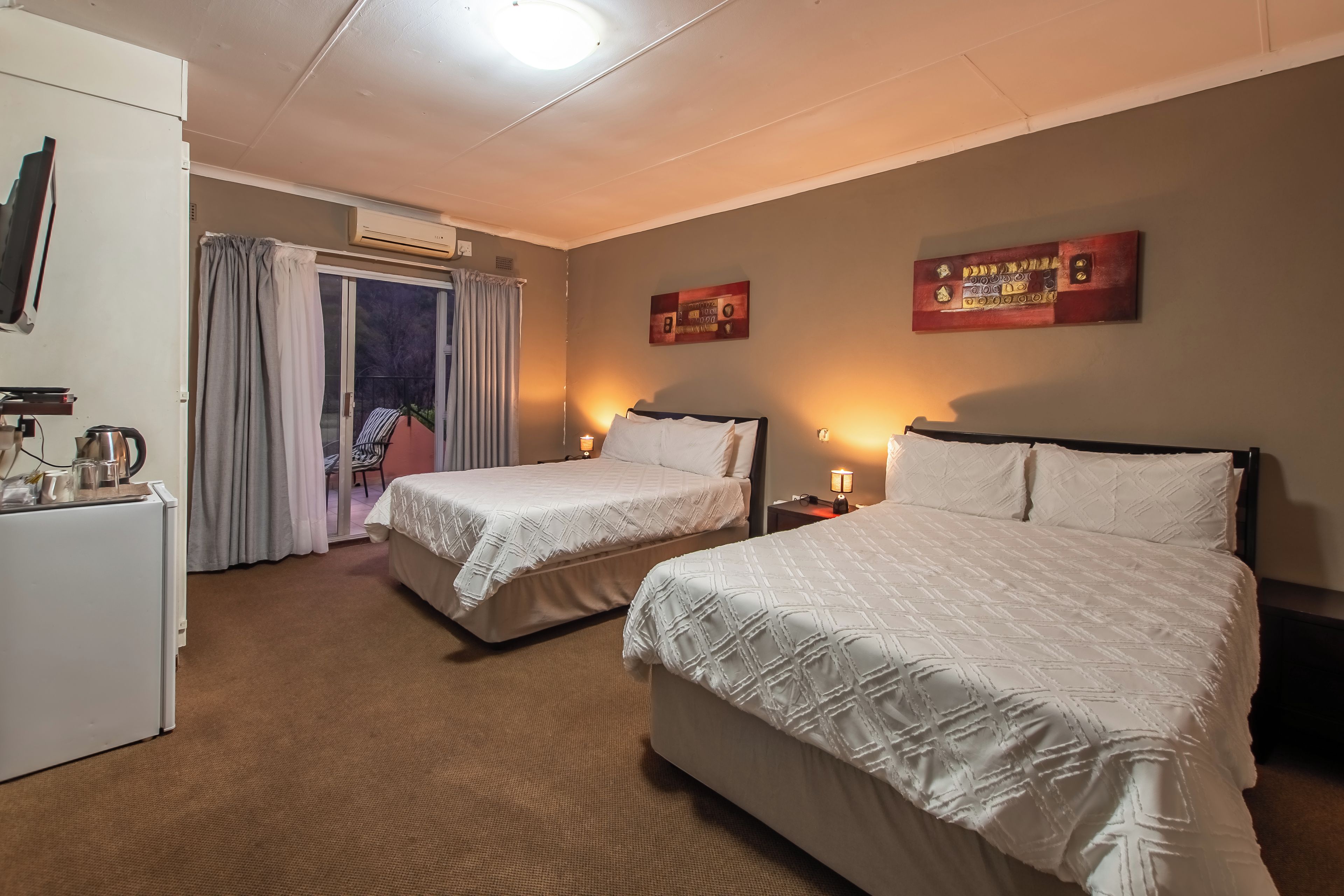 Habitación de hotel con dos camas, un escritorio con hervidor y vistas al exterior.