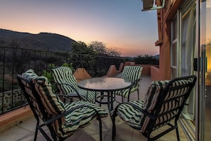 Terraço com mesa redonda e cadeiras listradas, com vista para uma paisagem montanhosa.