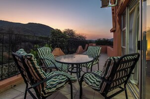 Una terraza con una mesa redonda y sillas a rayas, con vistas a un paisaje montañoso.