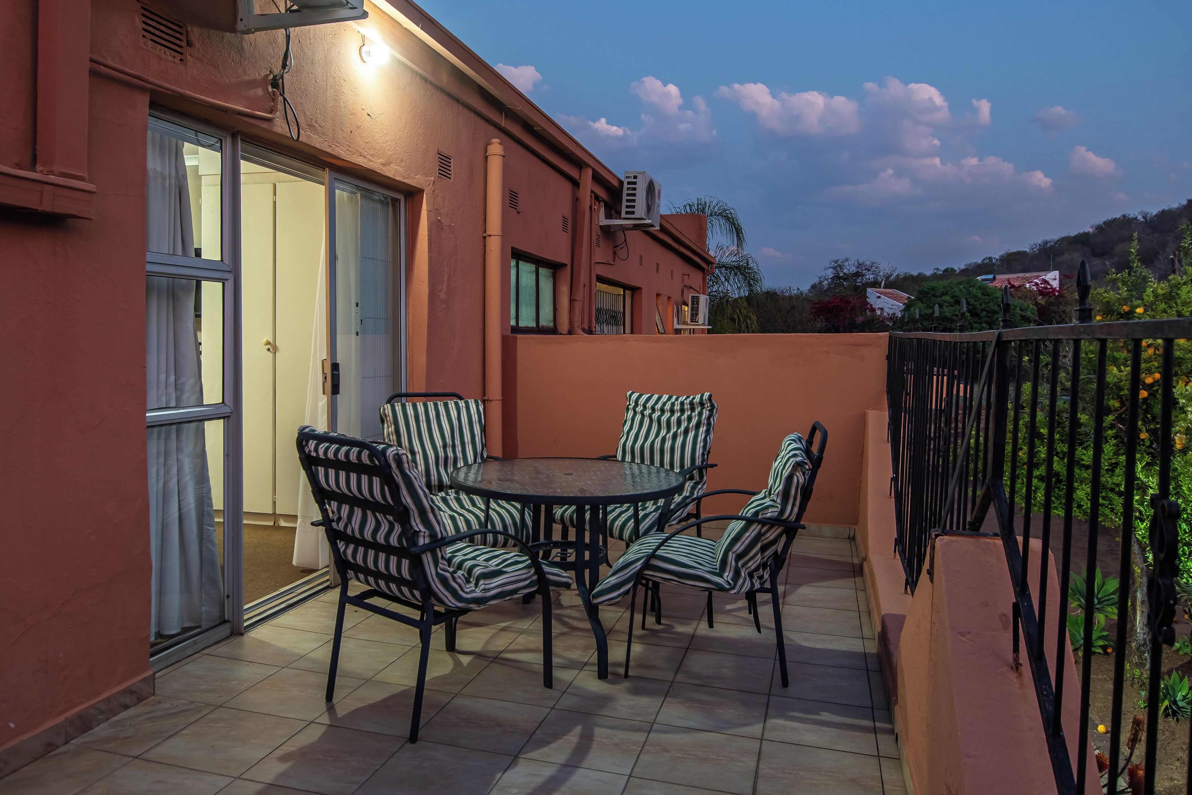 An outdoor patio with a round table and striped chairs, a sliding door, and an air conditioning unit.