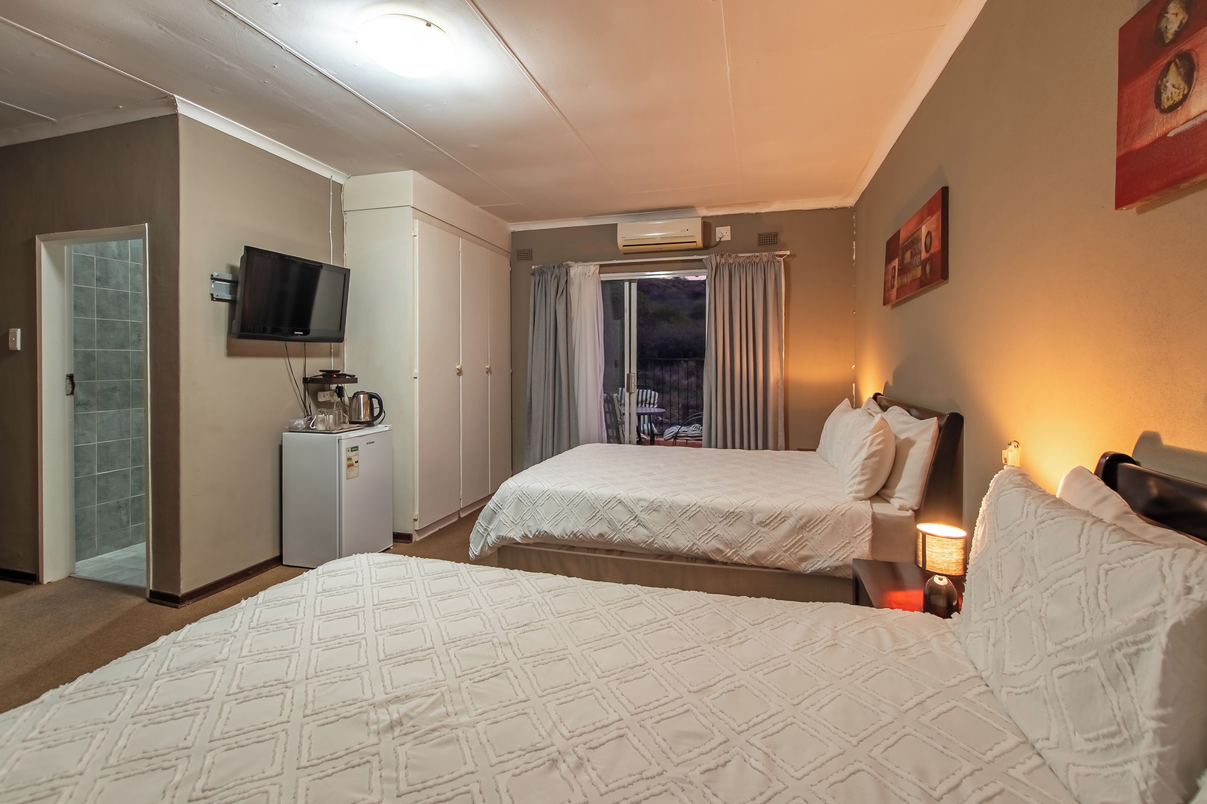 Een hotelkamer met twee bedden, een televisie, een koelkast en een raam met gordijnen.