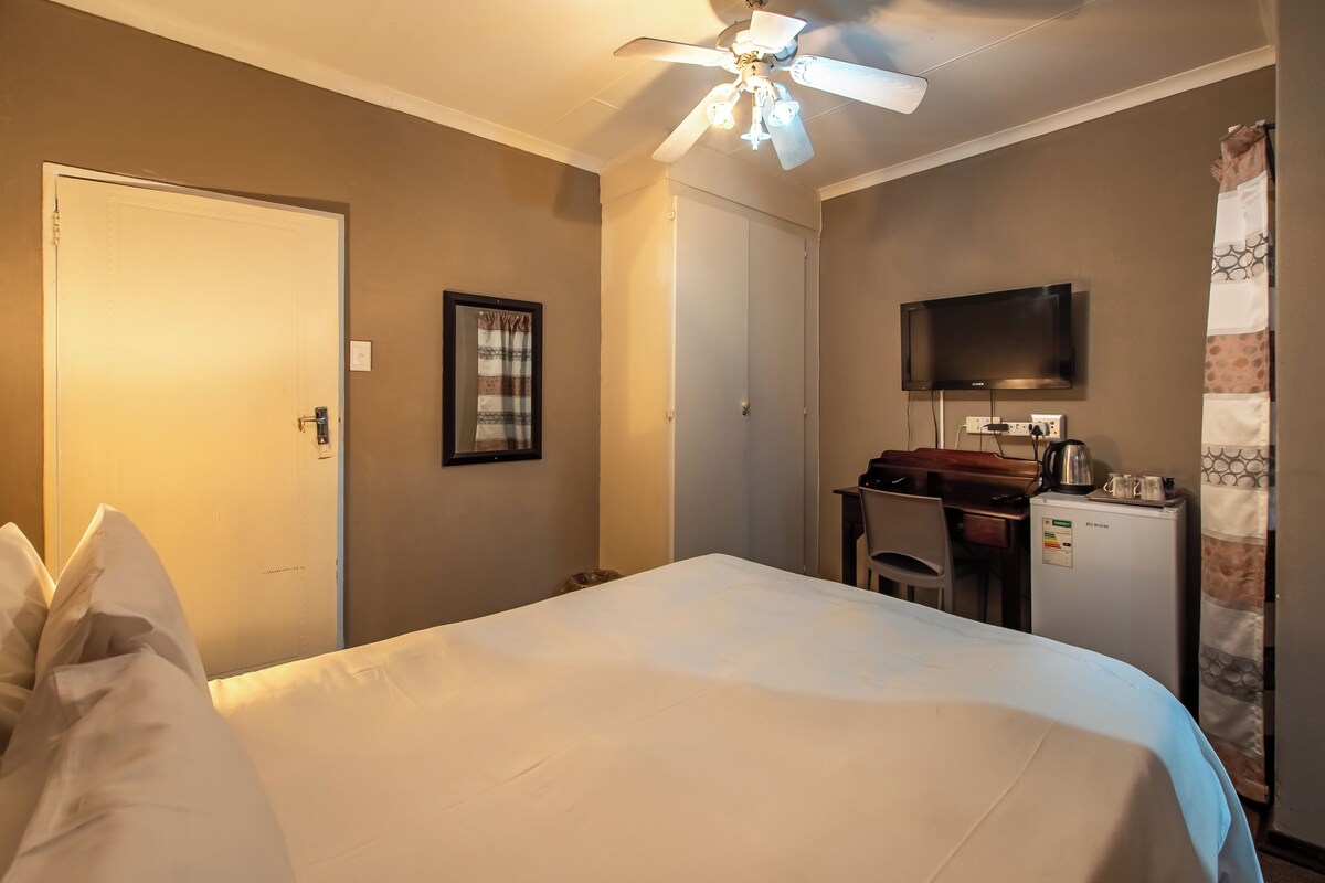 A hotel room with a bed, a desk with a computer, a television, and a ceiling fan.