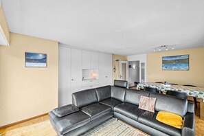 Ein modernes Wohnzimmer mit einer Ledersofa, einem Essbereich mit Tisch und Stühlen, und einer Küche im Hintergrund.