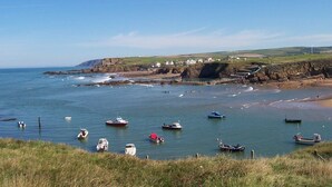 A coastal scene with boats on calm waters, a rocky shoreline, and buildings in the background. - Bude Surf Shack | Walk to the beach | Dog-friendly | Sleeps 5 (Bude)