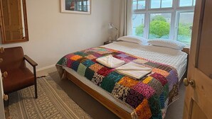 A bedroom with a bed, a chair, a rug, a window, and a painting on the wall. - Bude Surf Shack | Walk to the beach | Dog-friendly | Sleeps 5 (Bude)