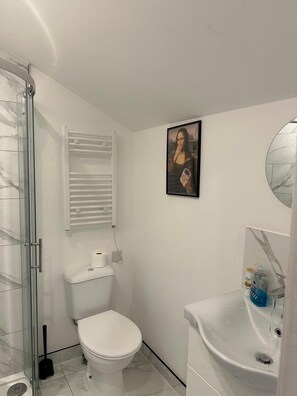 A bathroom with a glass shower enclosure, a toilet, a towel rack, a sink with a mirror, and a framed artwork on the wall. - Apartment Sleeps 3 Near High Street (Thornton Heath)