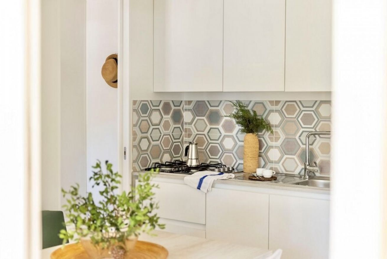 A modern kitchen with white cabinets, a hexagonal patterned backsplash, a gas stove, and a sink.
