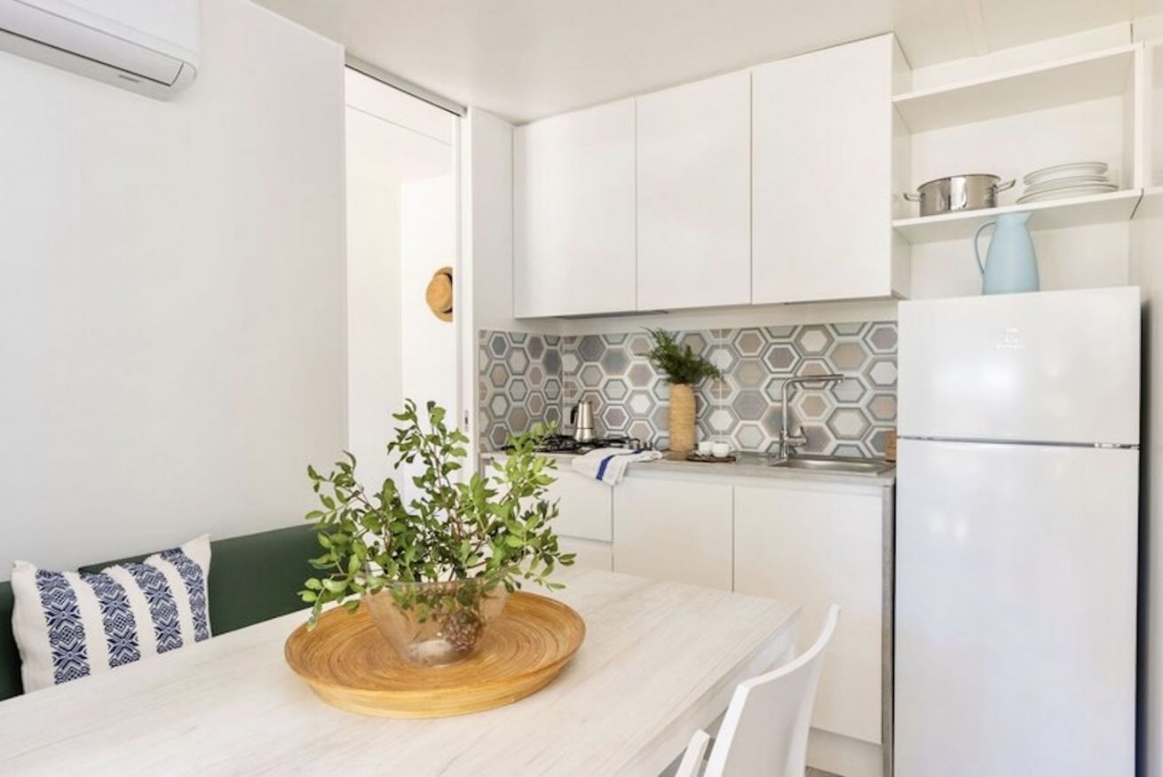 Cozinha moderna com armários brancos, painel hexagonal e geladeira embutida.