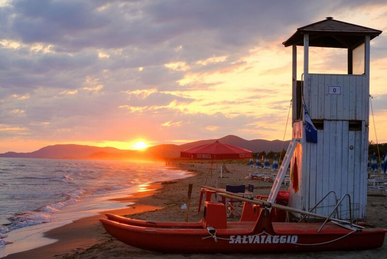 Una torre de socorristas, un bote salvavidas rojo y una sombrilla de playa.