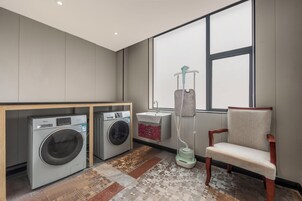 Una sala de lavandería con dos lavadoras, un lavabo, una silla y una ventana.