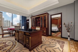 A hotel room with a large desk, a bed, a view of the city, and a decorative vase.