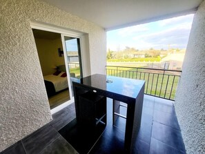 A balcony with a black table and chairs, a sliding glass door leading to a bedroom, and a view of a green landscape. - Hotel Le Capricorne Rest. Le Trianon (Marmande)