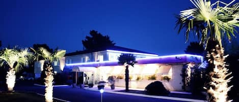 A hotel with a well-lit facade, palm trees, and a clear night sky.