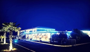 Ein Hotel mit auffälligem Restaurantschild, einem gut beleuchteten Eingang und einem Parkplatz.
