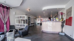 A modern hotel lobby with a reception desk, seating area, and a large vase on a table. - Hotel Le Capricorne Rest. Le Trianon (Marmande)