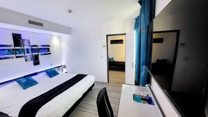 A modern hotel room with a bed, desk, and a large mirror. - Hotel Le Capricorne Rest. Le Trianon (Marmande)
