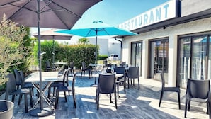 An outdoor patio with tables and chairs, a restaurant sign, and a hedge in the background. - Hotel Le Capricorne Rest. Le Trianon (Marmande)