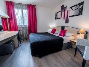 Habitación de hotel con cama, escritorio, silla y obras de arte en las paredes.