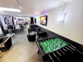 Un área de lounge moderna con una mesa de fútbol de mesa, asientos cómodos y una pantalla de televisión.
