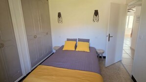 Un dormitorio con cama, dos almohadas, una mesita de noche y una puerta.