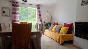 Un comedor con mesa y sillas, un sofá con cojines, una chimenea y una ventana con cortinas.